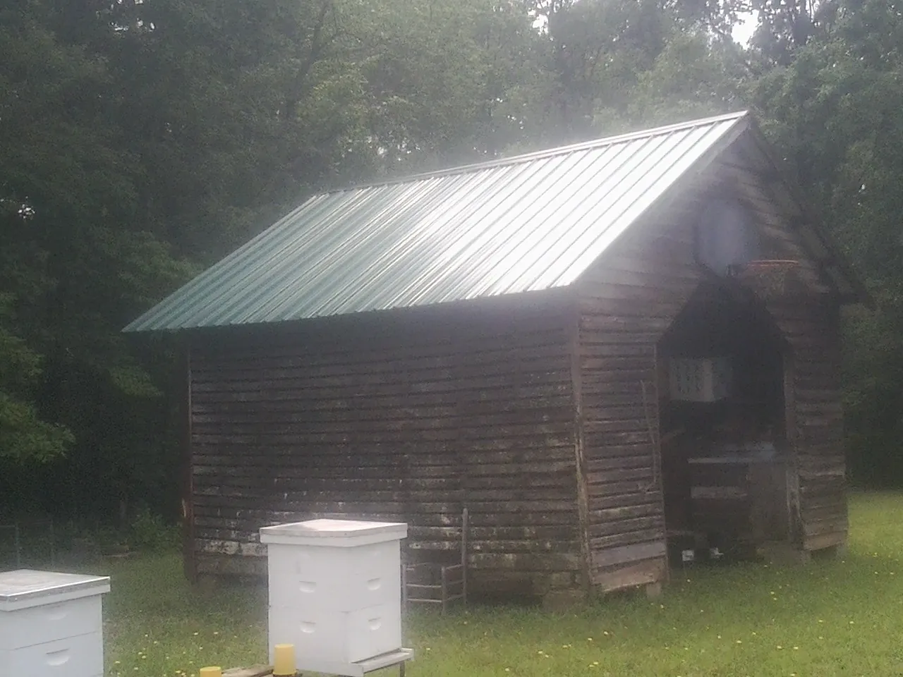 Green metal roof on a weathered barn beside stacked beehives in Bethlehem